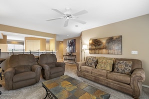 A living room with a brown sofa, two armchairs, a coffee table, and a ceiling fan.