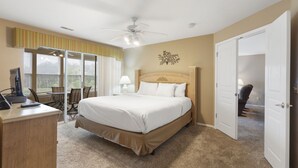 Un dormitorio con cama, escritorio, silla, ventilador de techo y vistas por una ventana.