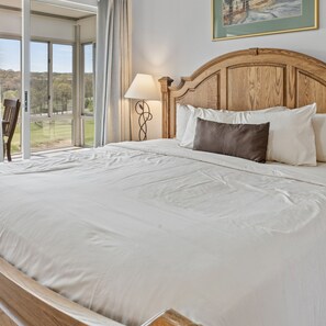 A large bed with white linens, a wooden headboard, and a view of a golf course through the window.