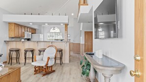 A modern kitchen with wooden cabinets, a bar area with stools, a white chair, and a large window. - 3 Bedroom, 3 Bath Golf Condo with Beautiful Course View from All-Season Sunroom (Branson)