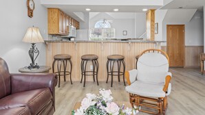 A modern kitchen with wooden cabinets, a bar area with stools, a dining chair, and a decorative lamp. - 3 Bedroom, 3 Bath Golf Condo with Beautiful Course View from All-Season Sunroom (Branson)