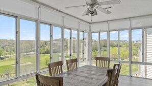 A dining area with a large table and chairs, large windows, and a ceiling fan. - 3 Bedroom, 3 Bath Golf Condo with Beautiful Course View from All-Season Sunroom (Branson)