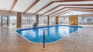Una piscina interior con suelo de ladrillo, vigas de madera y grandes ventanales.