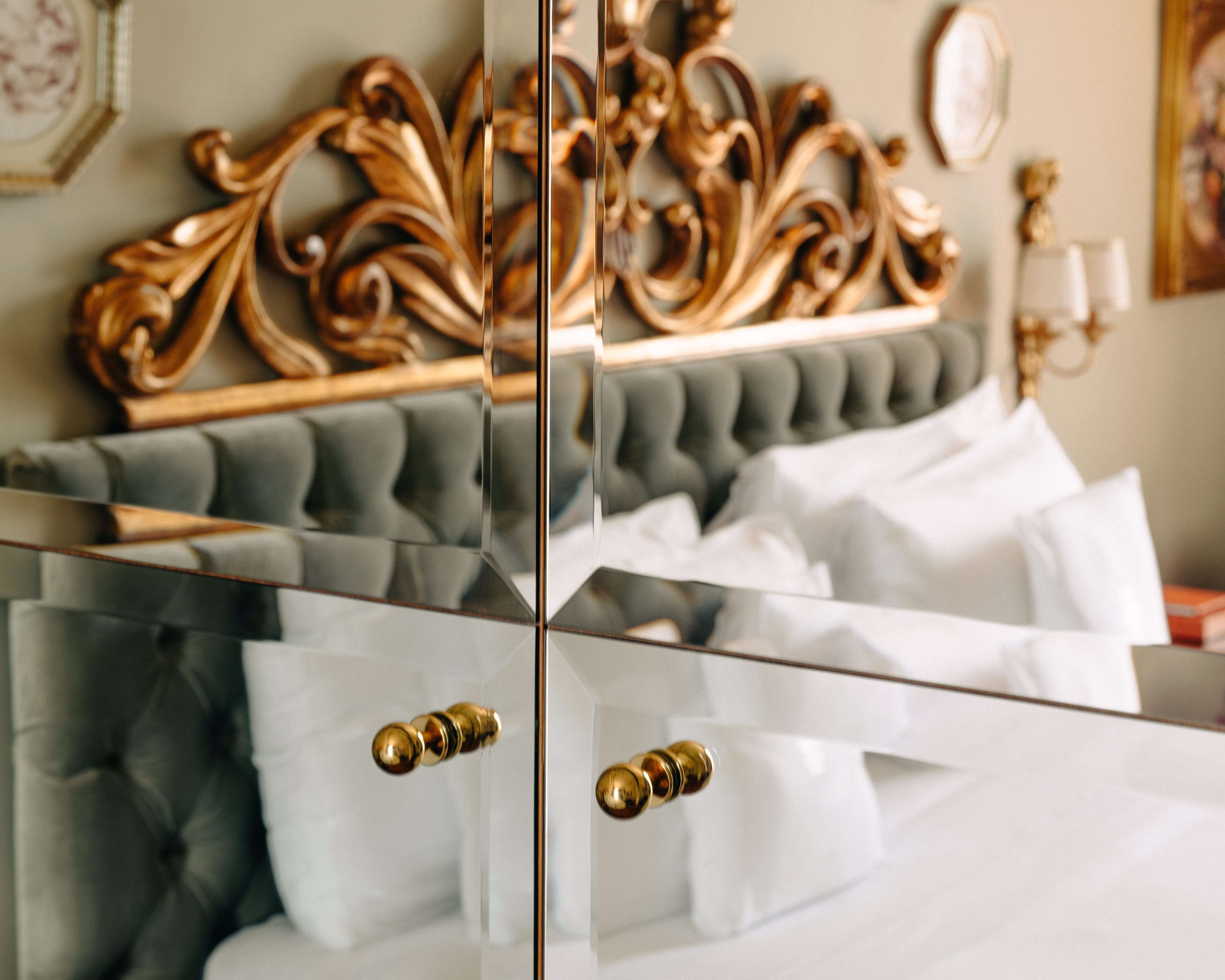 A bedroom with a tufted headboard, a mirror, and a bedside table with a lamp.