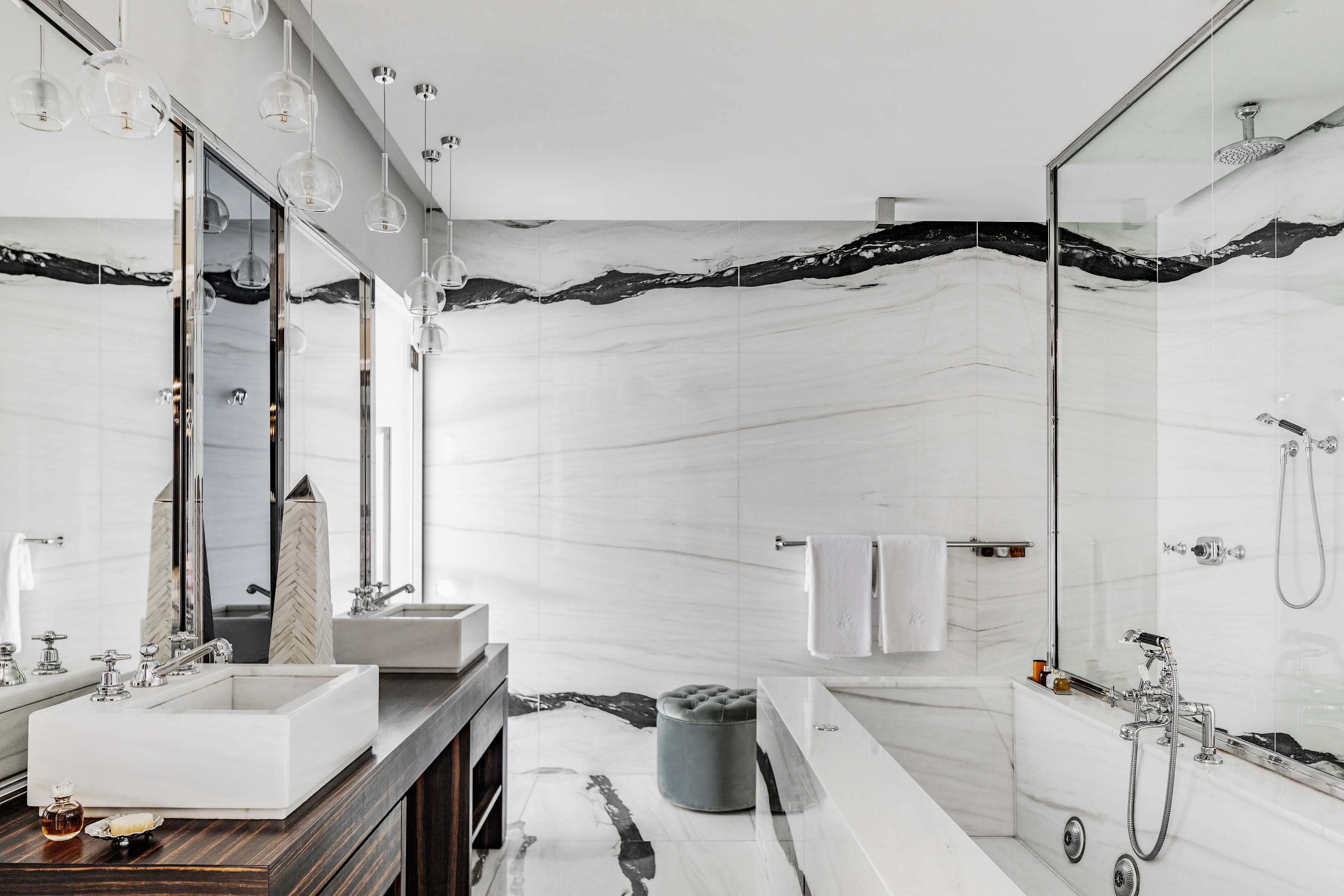 A modern bathroom with a large mirror, two sinks, a bathtub, and a shower.