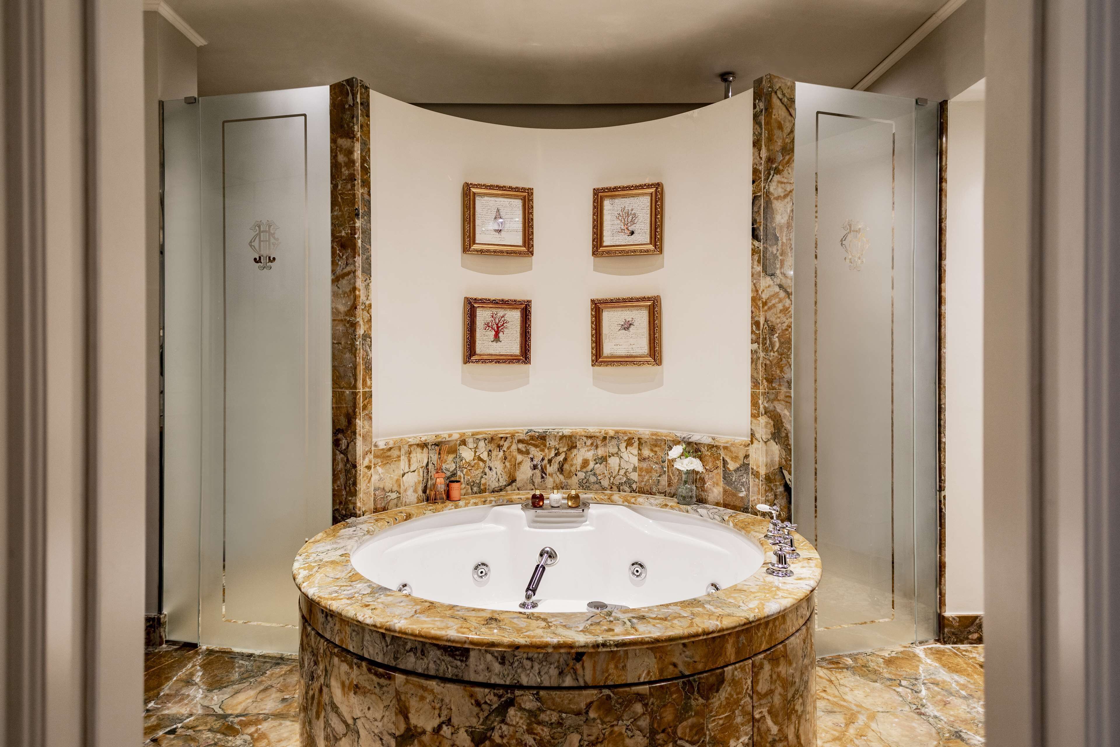 A luxurious bathroom with a large marble bathtub, framed artwork on the wall, and a marble vanity.