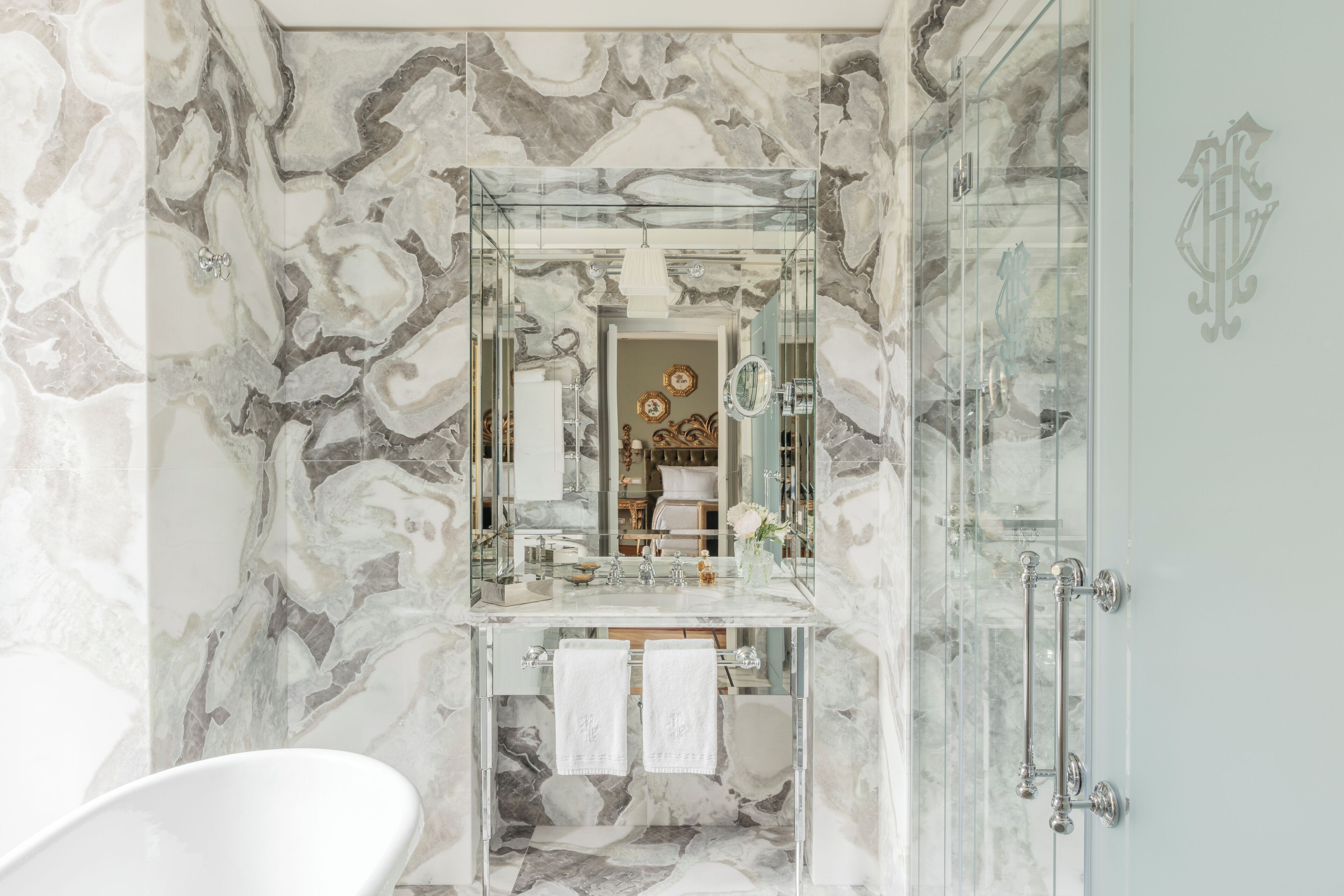 A bathroom with a marble wall, a glass shower enclosure, and a white bathtub.