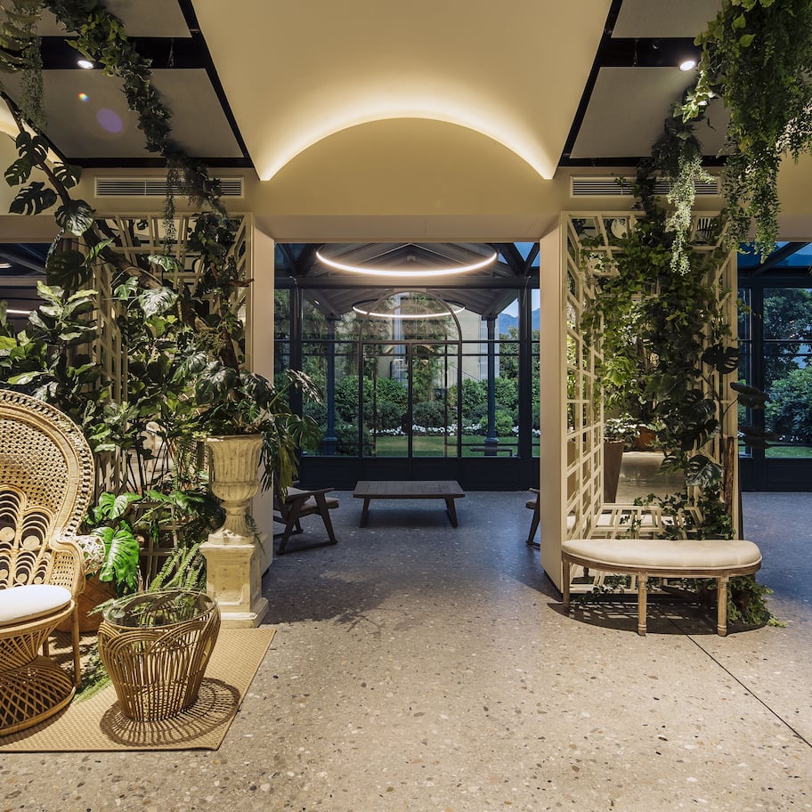 A spacious room with a large window, a wicker chair, a wooden bench, and potted plants.