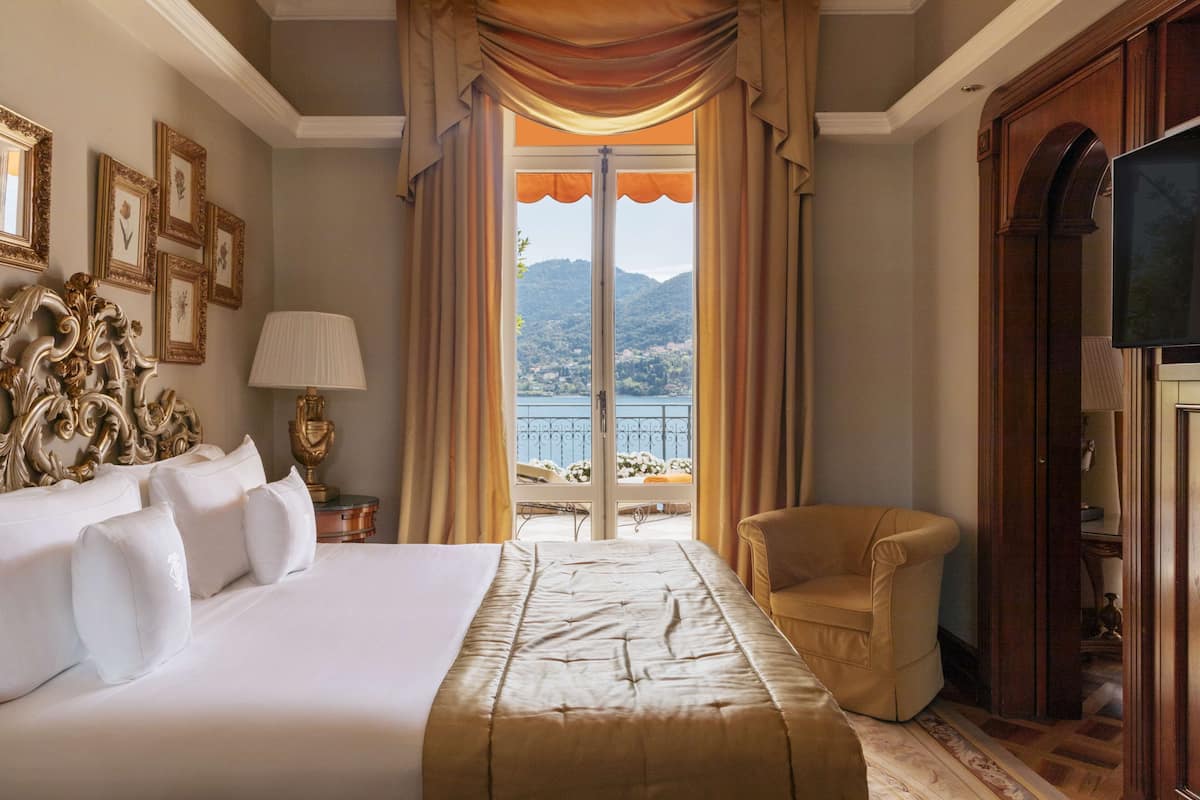 A hotel room with a large bed, a chair, a TV, and a balcony with a view of the mountains.