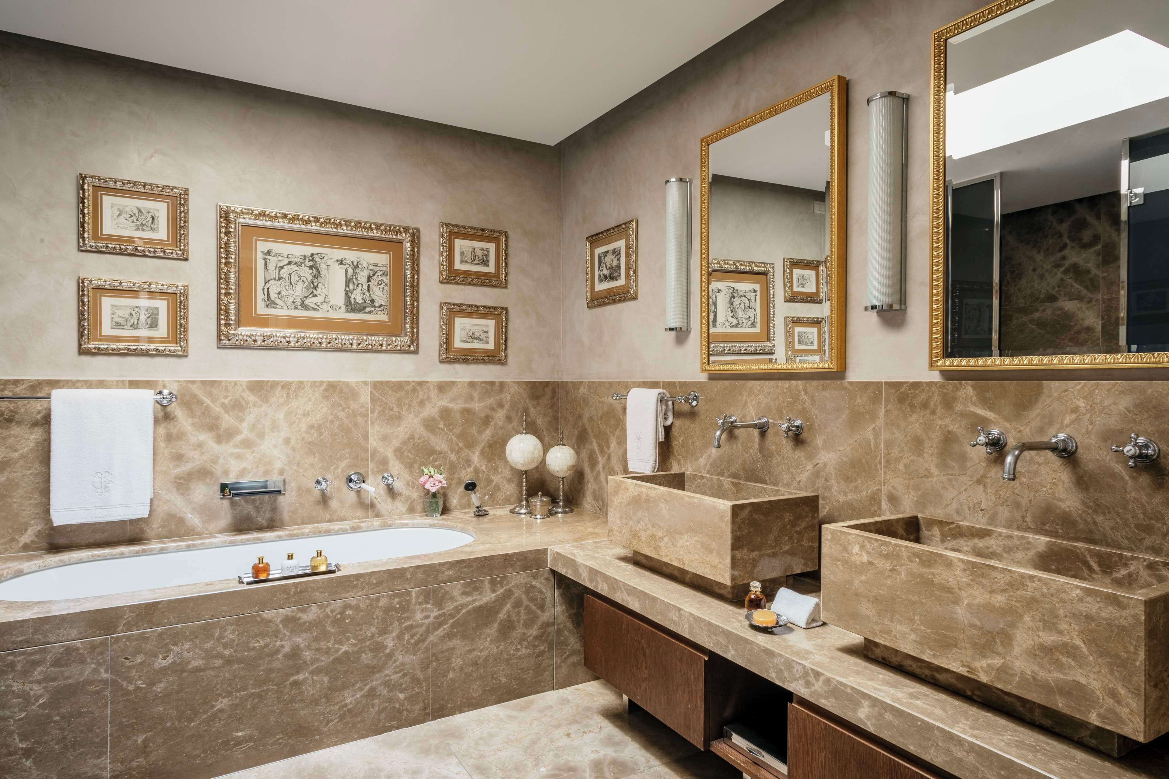 Une salle de bain dotée d’une grande baignoire, de deux lavabos, de murs en marbre et de tableaux encadrés.