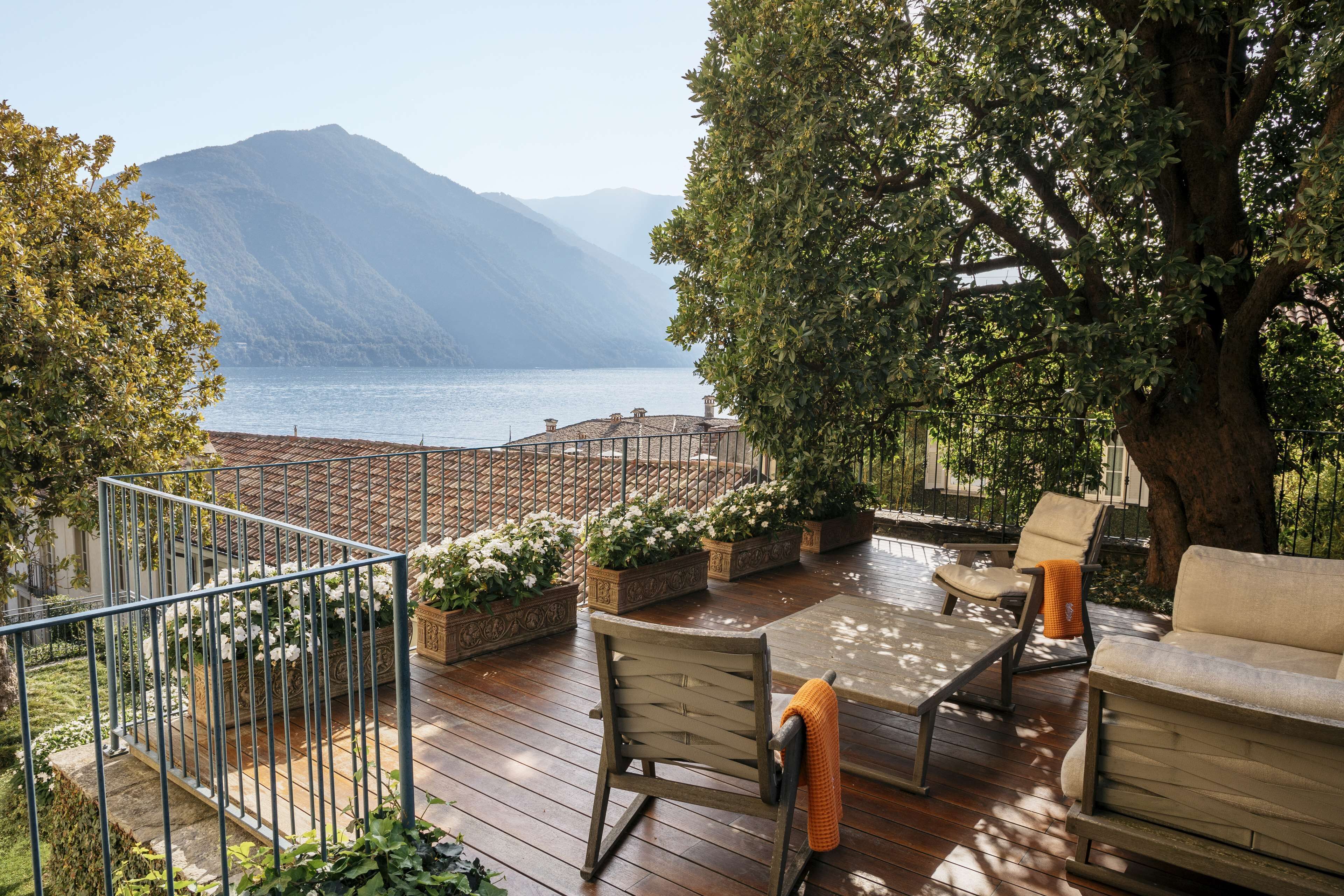 Una terrazza con mobili da esterno, piante in vaso e vista su un lago e montagne.