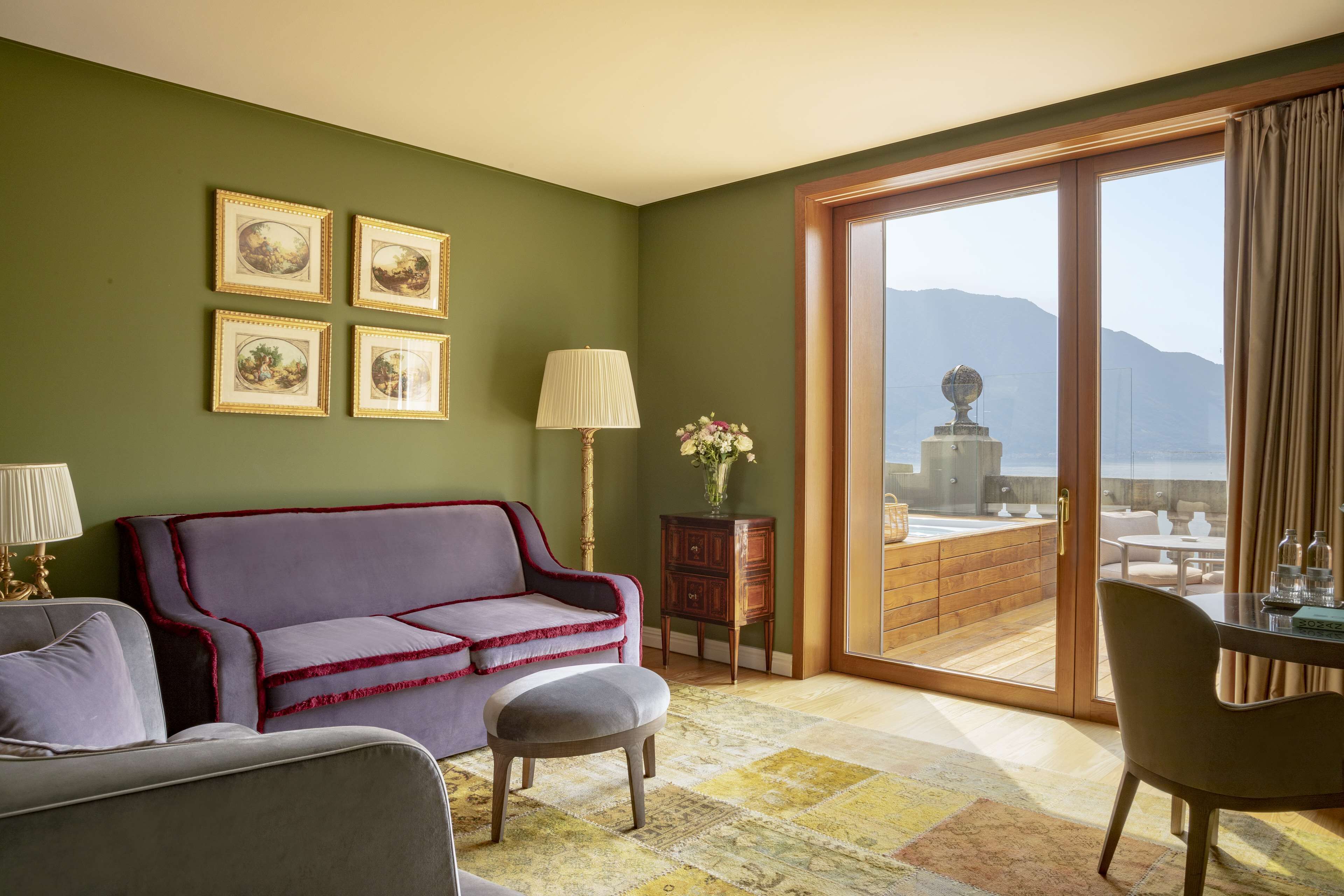 A room with a green wall, a purple sofa, a small table with a lamp, and a view of mountains through a sliding door.