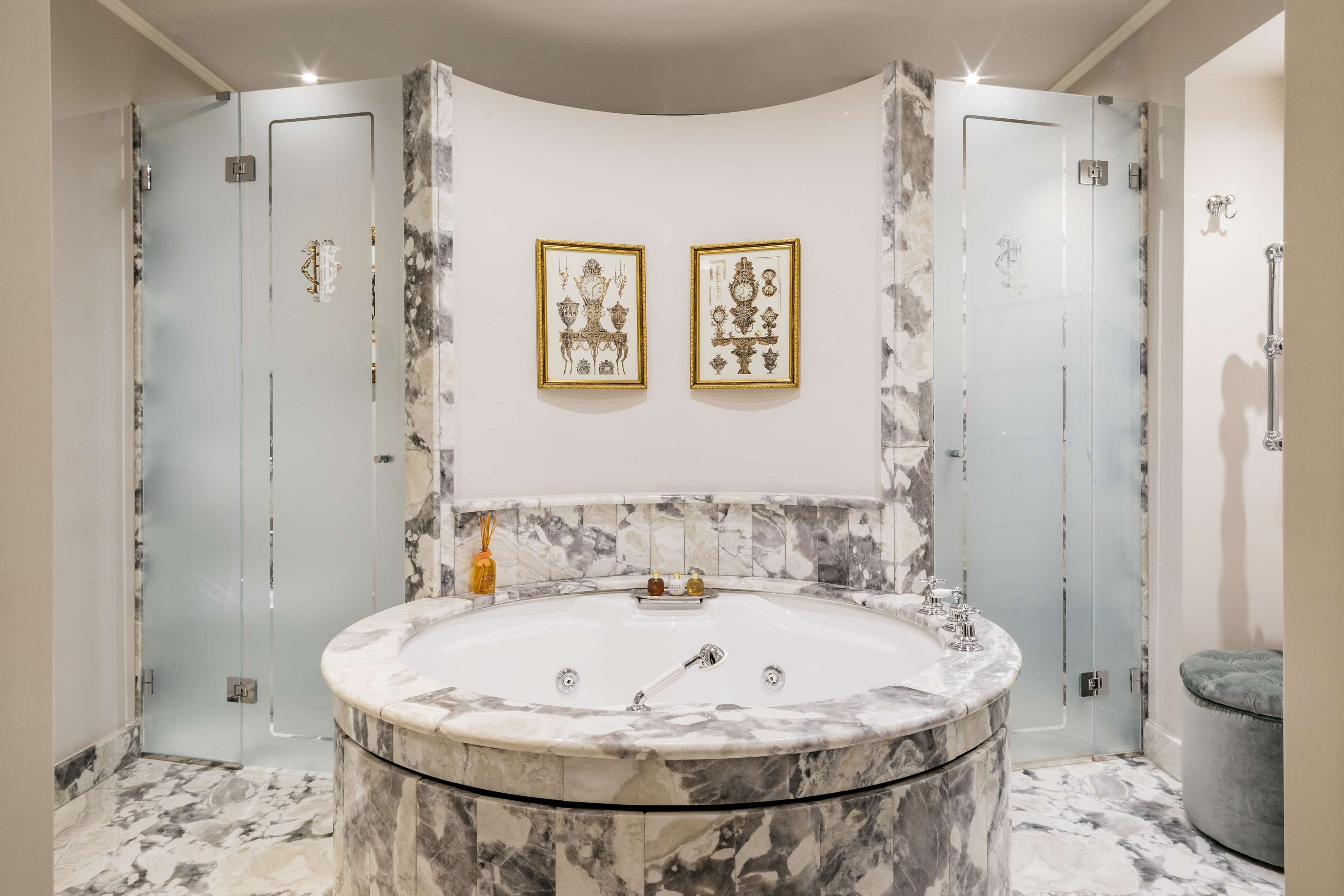 Ein luxuriöses Badezimmer mit einer großen Marmorbadewanne, zwei gerahmten Kunstwerken an der Wand und einem Marmorboden.