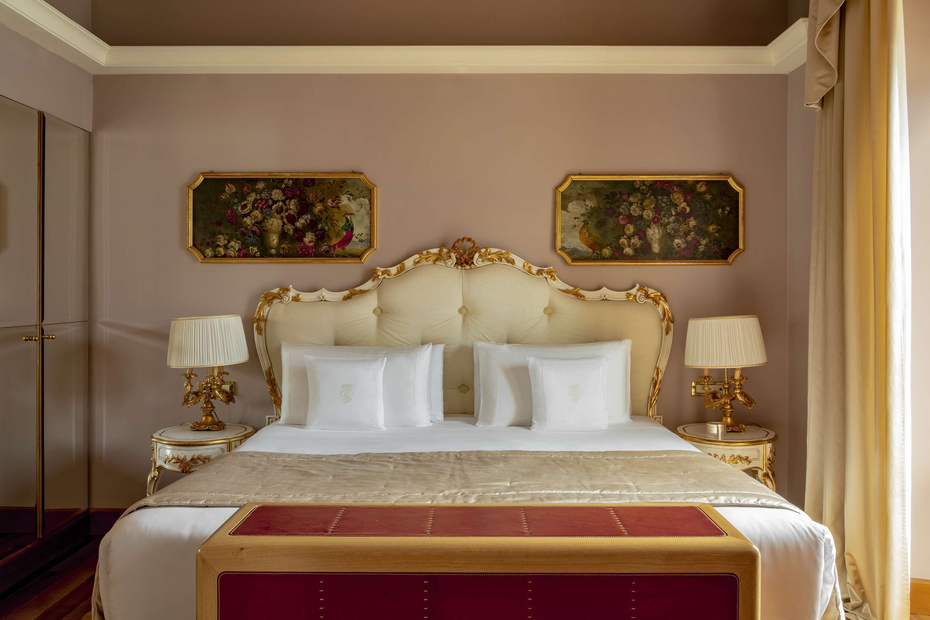 A large bed with a tufted headboard, two bedside tables with lamps, and two framed floral paintings on the wall.