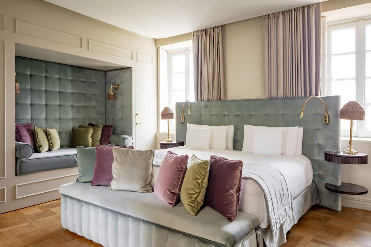 A bedroom with a large bed, a seating area, and a window with curtains.