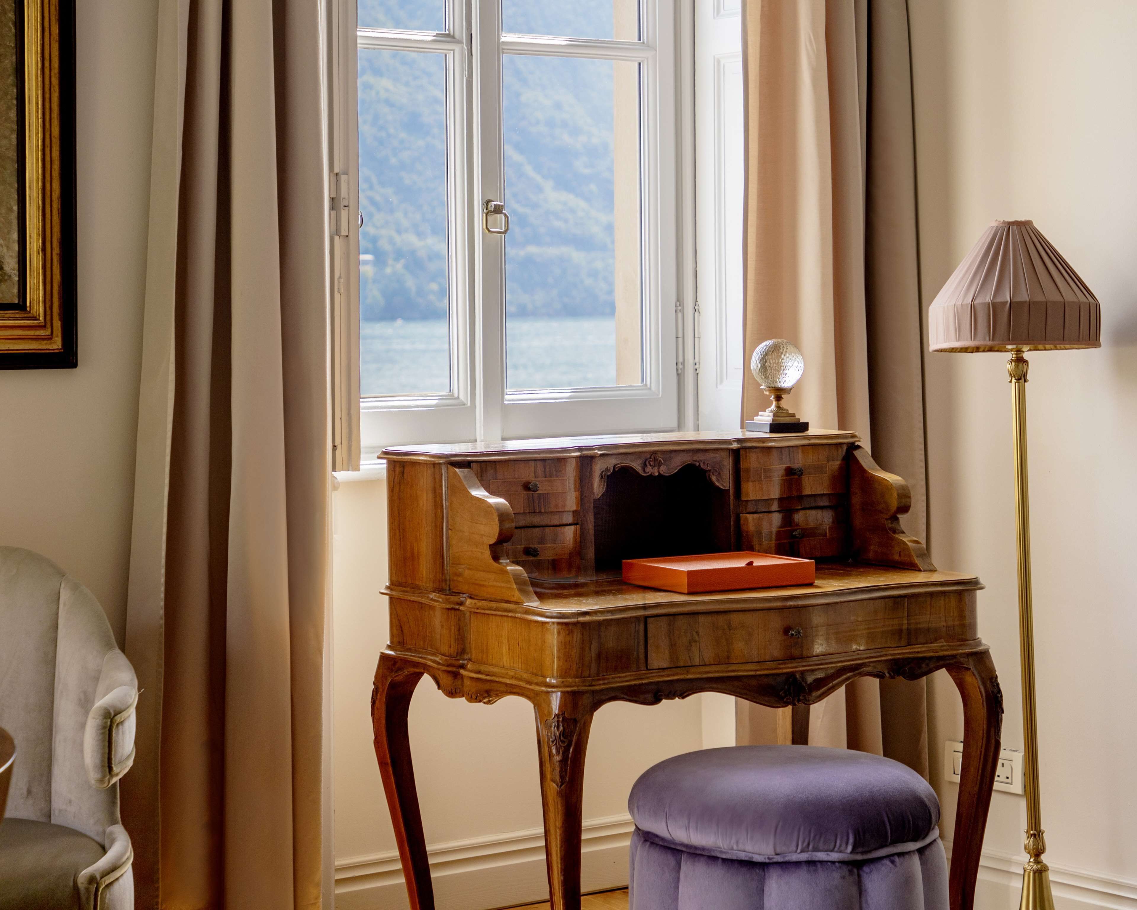 A room with a wooden desk, a lamp, a chair, and a window with a view of the sea.