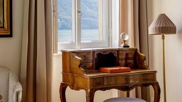 A room with a wooden desk, a lamp, a chair, and a window with a view of the sea.