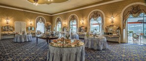 A luxurious banquet hall with ornate decor, large windows, and a view of the outdoors.