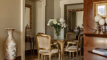 Un comedor elegante con una mesa de vidrio, sillas doradas y un jarrón grande con flores blancas.