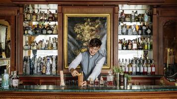 Un bar con un bartender preparando una bebida, rodeado de estantes llenos de botellas de licor.