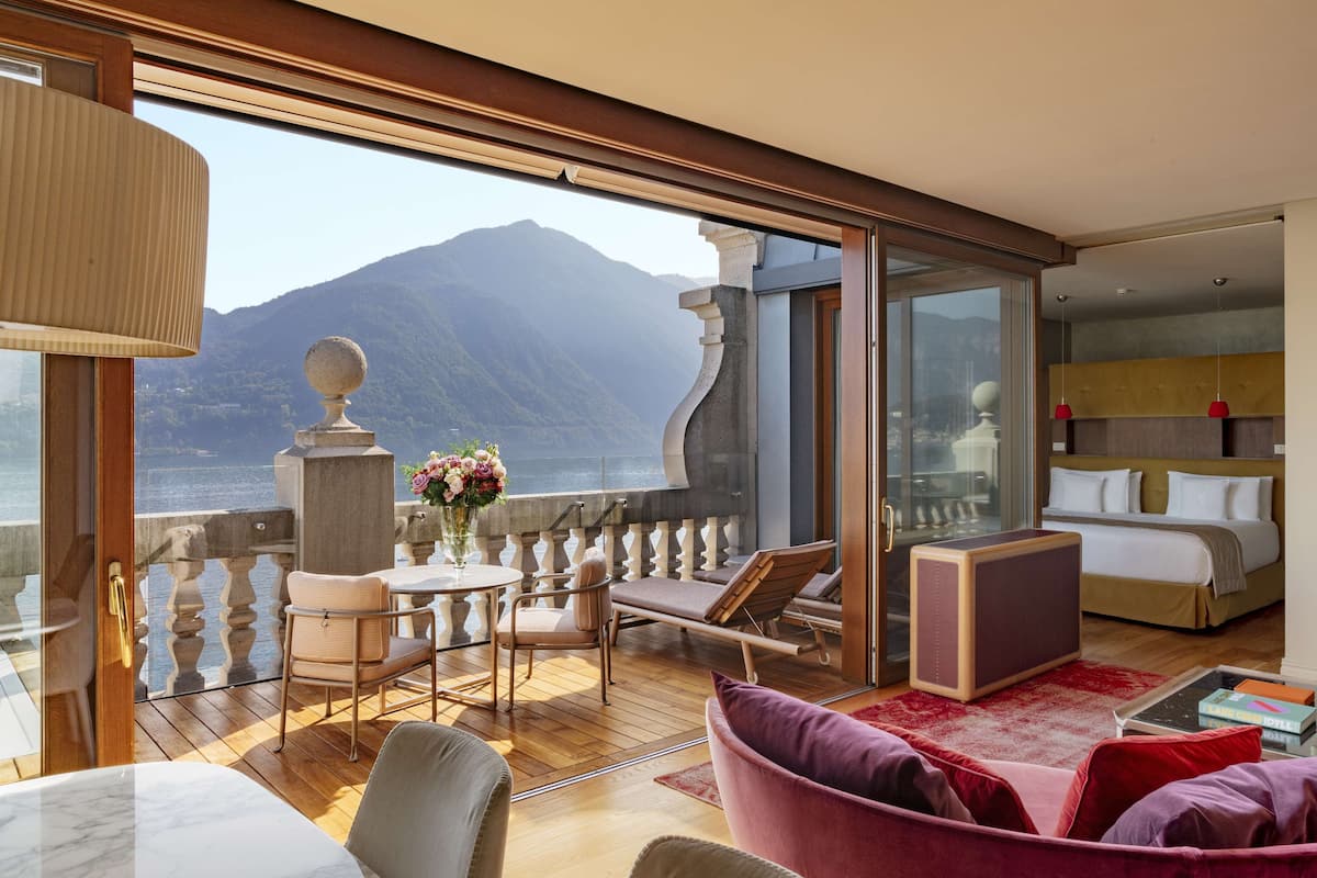 A balcony with a view of mountains and a body of water, furnished with a table, chairs, and a sofa.