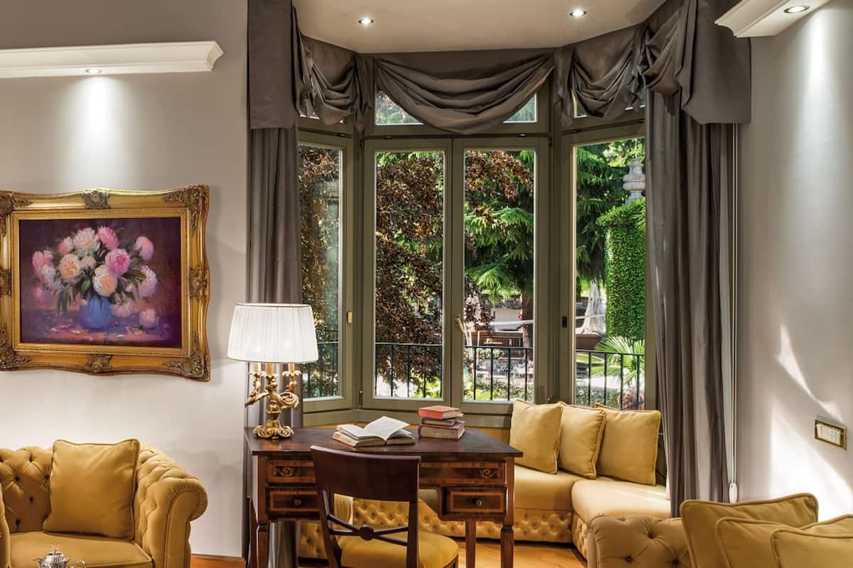 A well-lit living room with a dining area, large windows with curtains, and a painting on the wall.