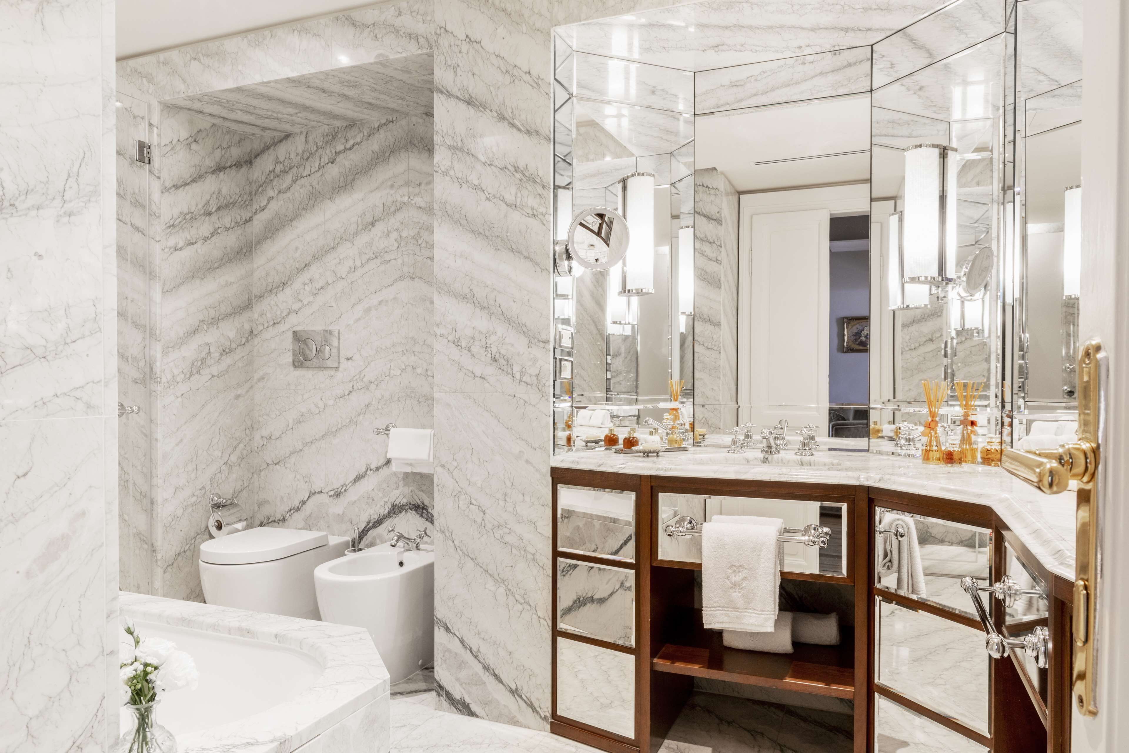 A modern bathroom with a marble wall, a freestanding bathtub, a vanity with a mirror, and a toilet.