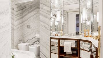 A modern bathroom with a marble wall, a freestanding bathtub, a vanity with a mirror, and a toilet.