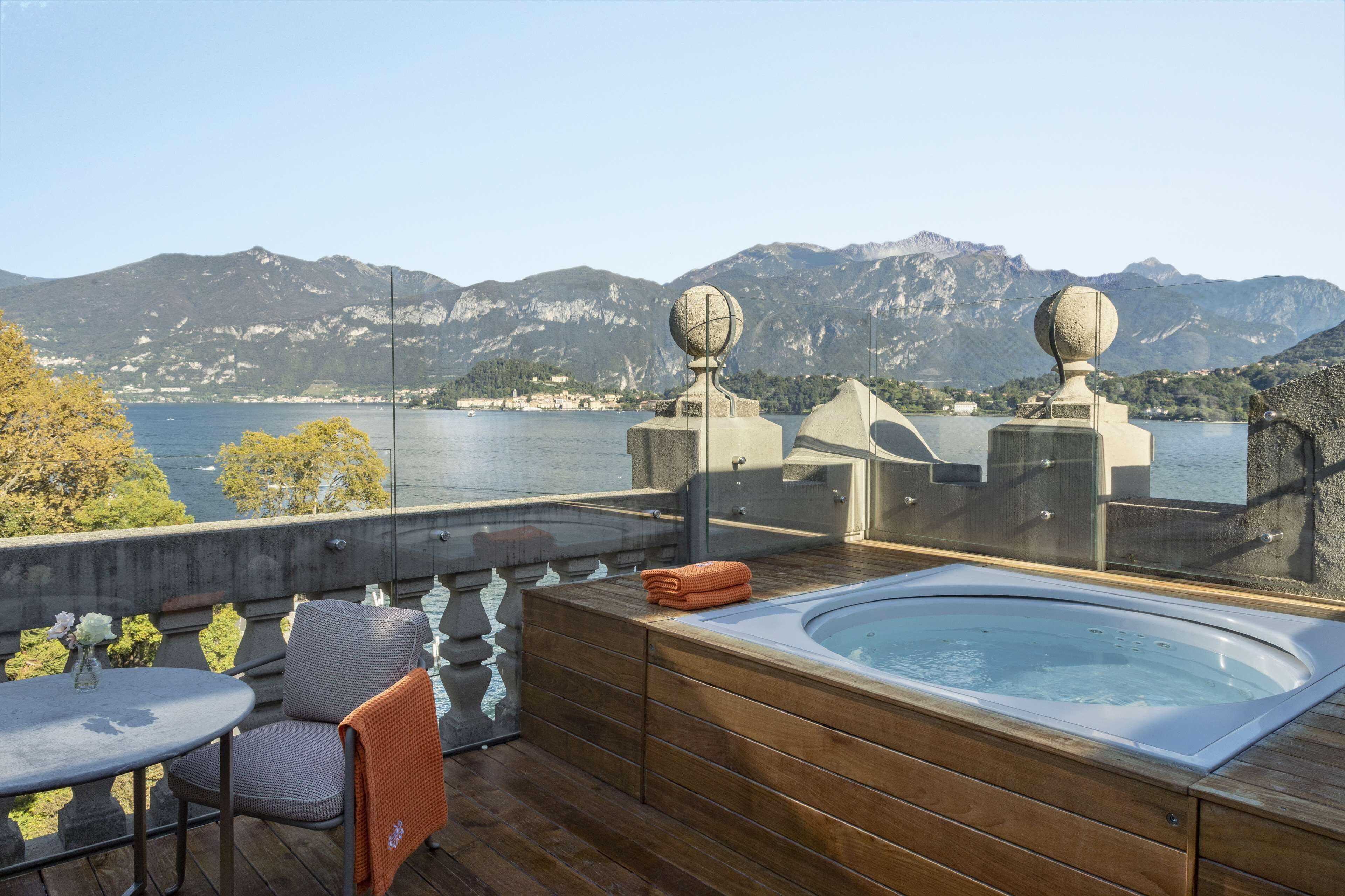 A rooftop terrace with a hot tub, seating area, and a view of a lake and mountains.