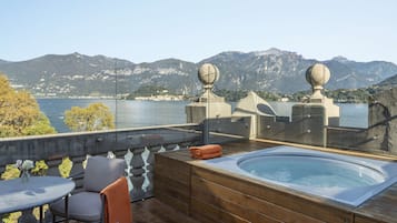 A rooftop terrace with a hot tub, seating area, and a view of a lake and mountains.