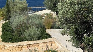A landscaped garden with various shrubs and a stone wall, overlooking a body of water. - Alon Sevou Boutique Hotel (Igoumenitsa)