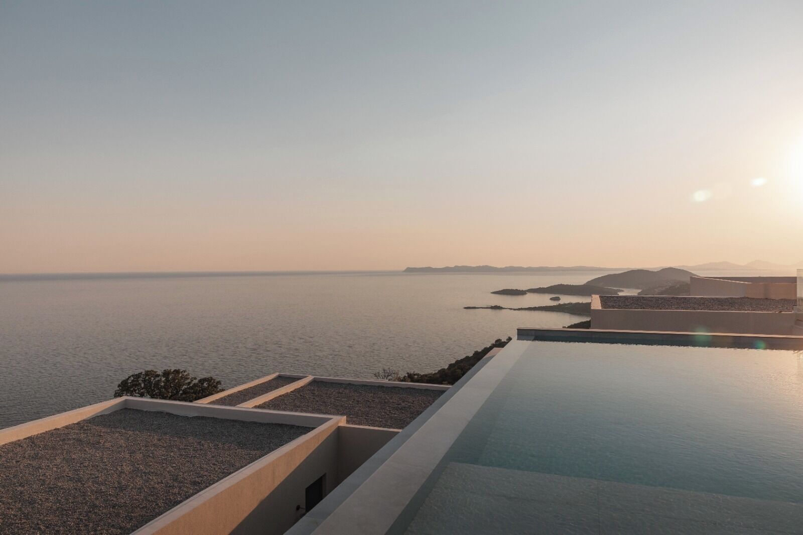 Une piscine à débordement moderne, offrant une vue imprenable sur une mer calme et sur des reliefs lointains.