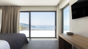 A modern hotel room with a large bed, a desk with a bowl, and a sliding glass door leading to a balcony with a view of the sea. - Alon Sevou Boutique Hotel (Igoumenitsa)
