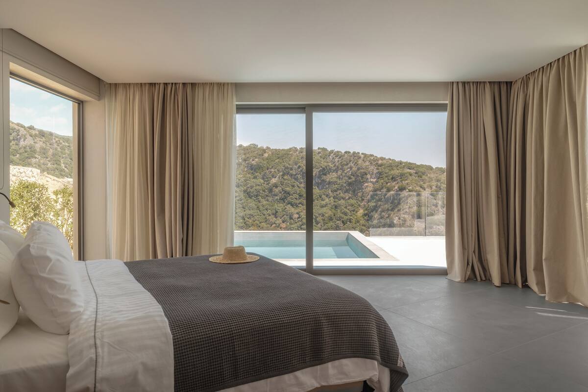 Ett modernt hotellrum med en stor säng, utsikt över ett bergigt landskap och en swimmingpool.