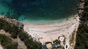 An aerial view of a coastal area with a beach, rocky terrain, and a small building with a green roof. - Alon Sevou Boutique Hotel (Igoumenitsa)