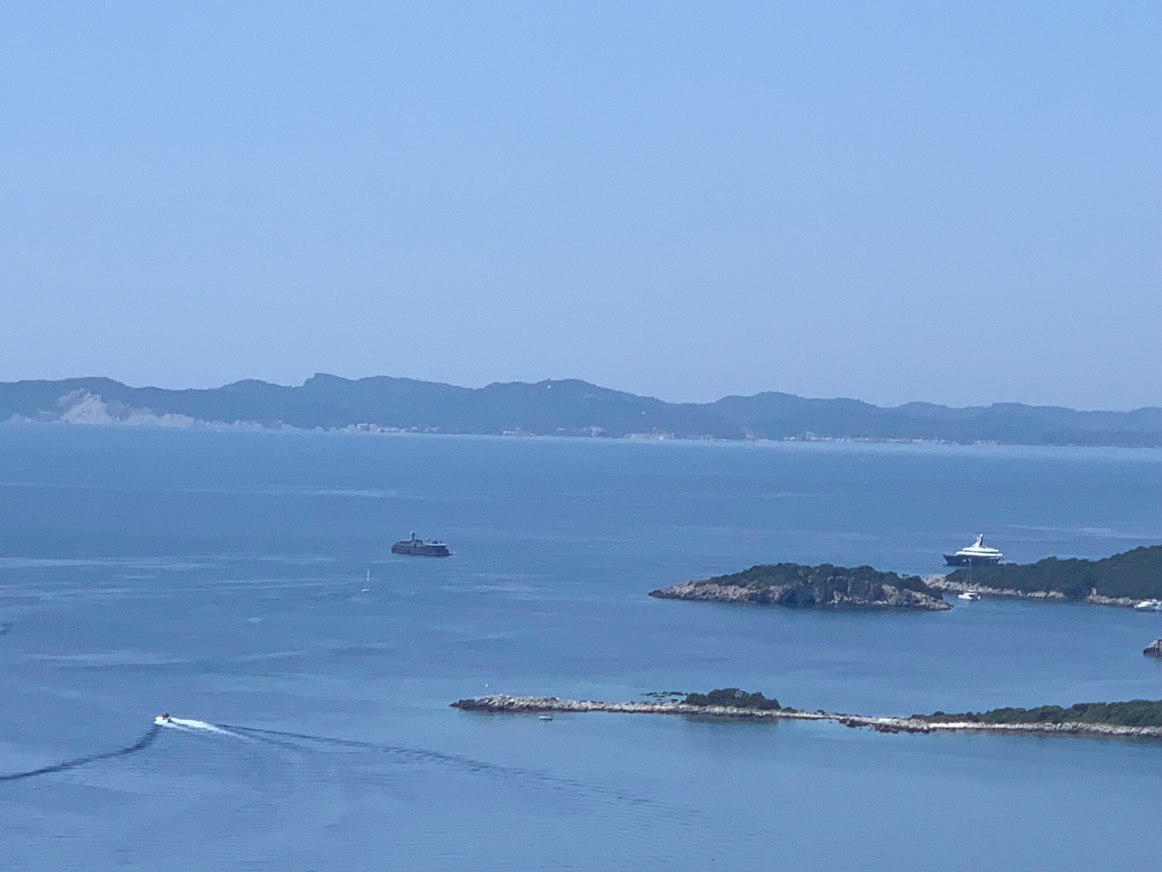 A coastal view with a ferry, a lighthouse, and distant mountains.