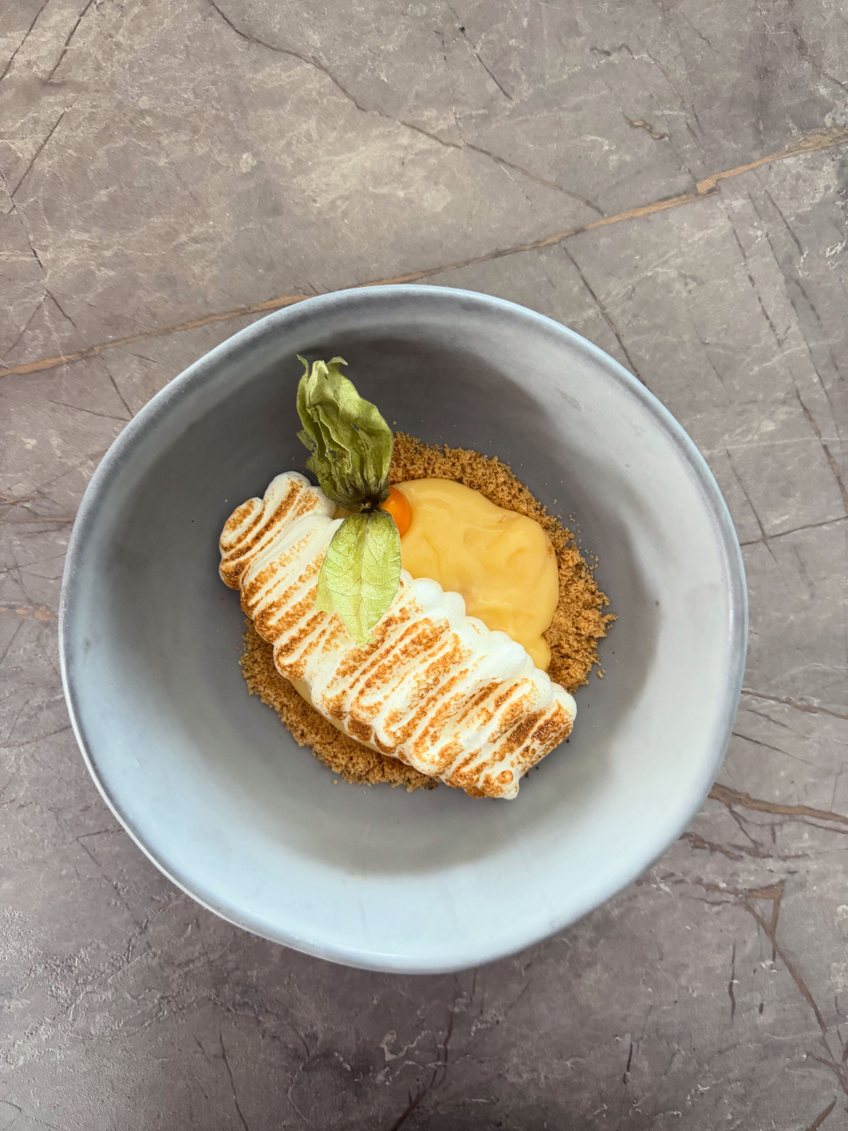 A bowl with a dessert featuring a waffle, a dollop of cream, and a green leaf garnish.