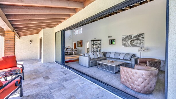 Una sala moderna con un sofá seccional, un reposapiés tapizado y un ventanal de vidrio que da a un patio exterior.