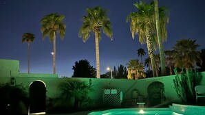 Un área de piscina nocturna con palmeras y un cielo despejado.