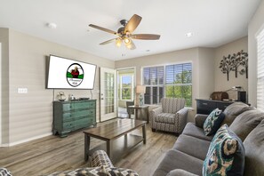 A spacious living room with a ceiling fan, a green dresser, a gray sofa, and a patterned armchair. - Walk-in Golf Condo with All-Season Sunroom, Beautiful Course View (Branson)