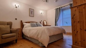 Quarto com cama, cadeira, guarda-roupa de madeira e janela com cortinas.