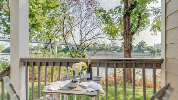 Eine Holzterrasse mit Tisch für Zwei, mit Blick auf einen Fluss und eine Brücke.