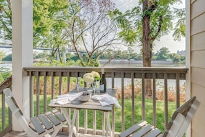 A wooden deck with a table set for two, overlooking a river and a bridge.