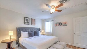 Ein Schlafzimmer mit Bett, Nachttischen, Deckenventilator und Bildern an den Wänden.
