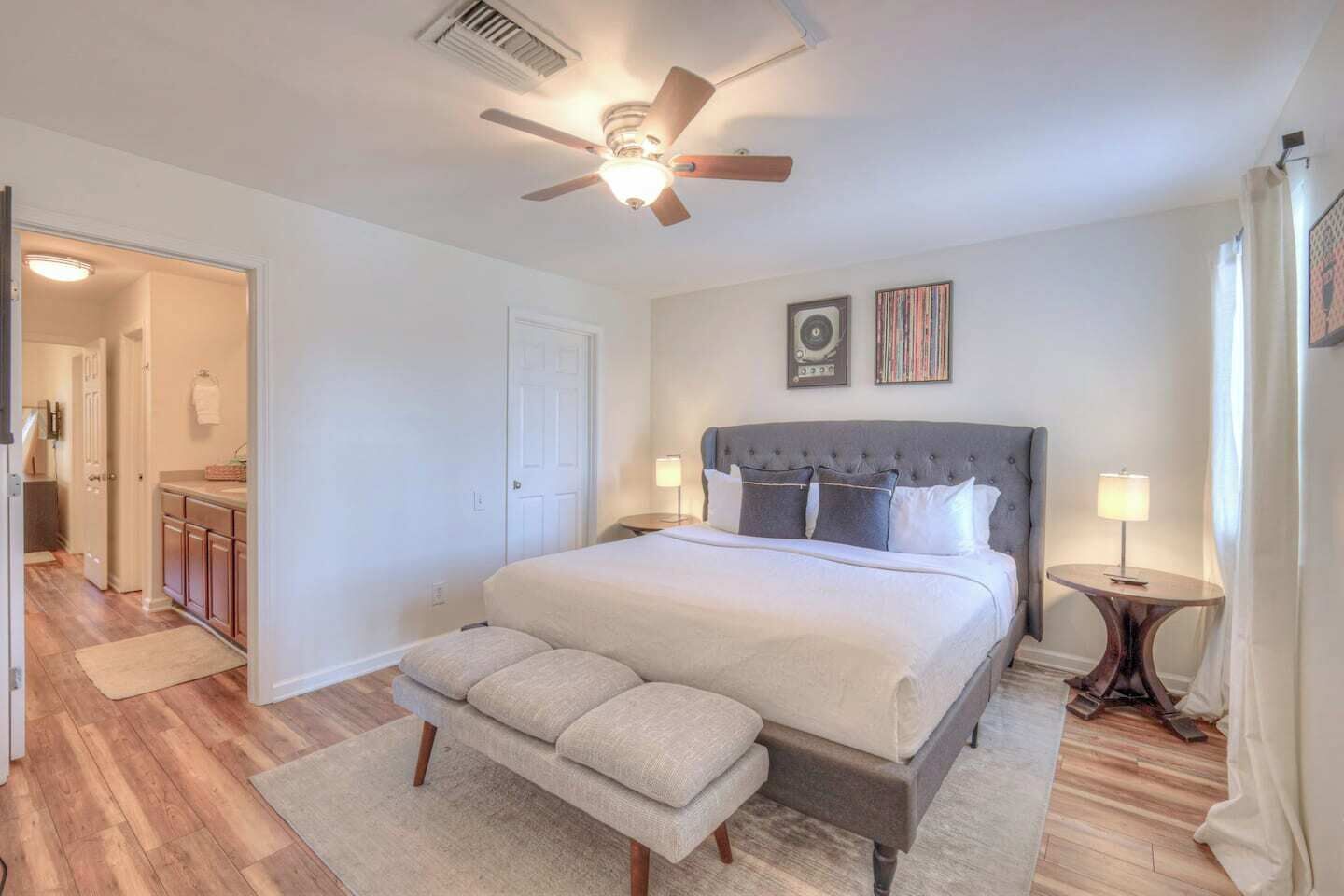 A bedroom with a large bed, a ceiling fan, a bedside table with a lamp, and a door leading to a bathroom.