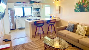 A modern kitchen with a central island, bar stools, a glass coffee table, and a sofa with patterned cushions. -  2-bedroom-ocean & St Croix views-5 minutes to Cruz Bay (Cruz Bay)
