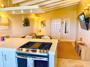 A modern kitchen with an island, a dining area with a sofa, a TV mounted on the wall, and a door leading to another room.