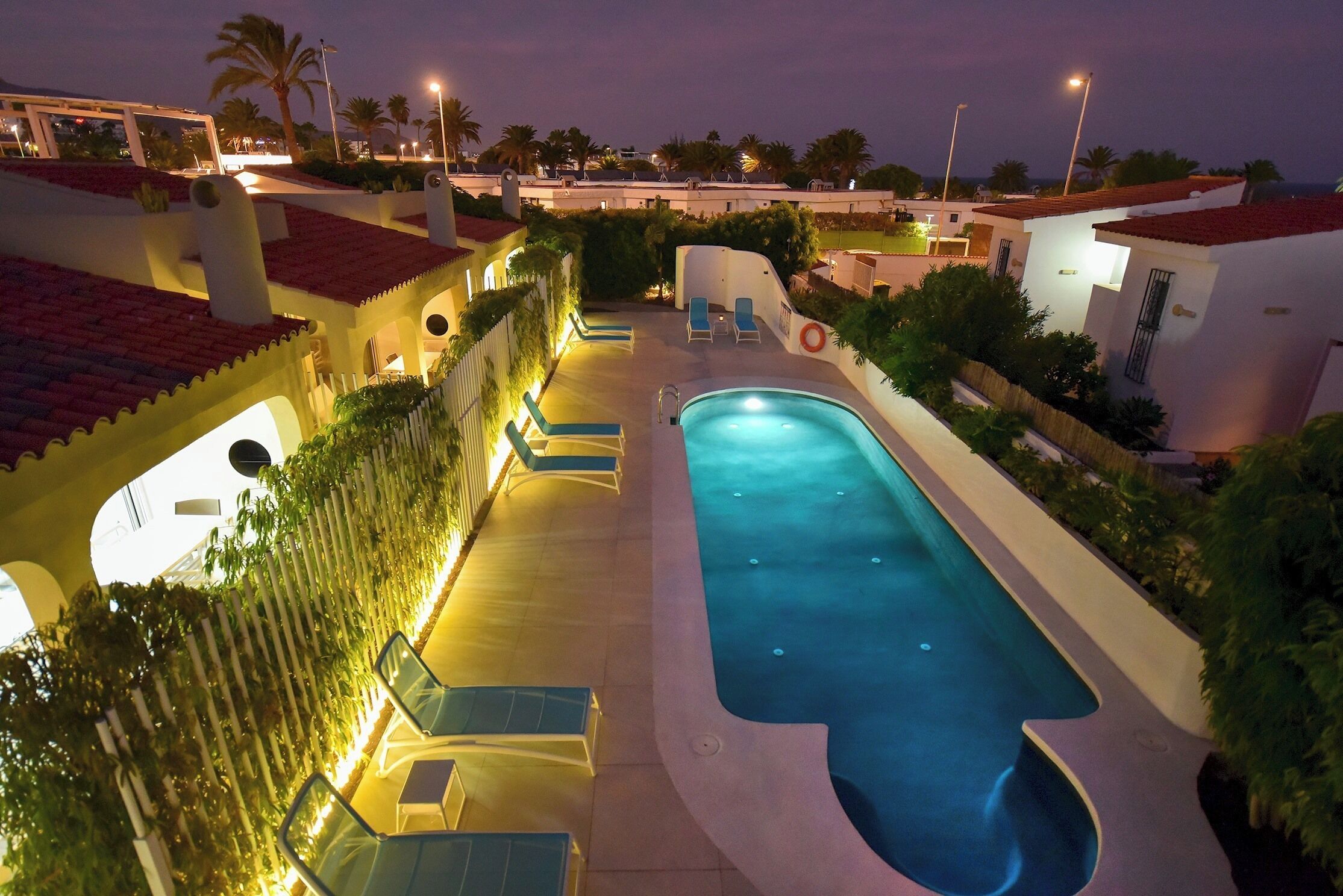 Piscina con sillones reclinables y un sendero bien iluminado.