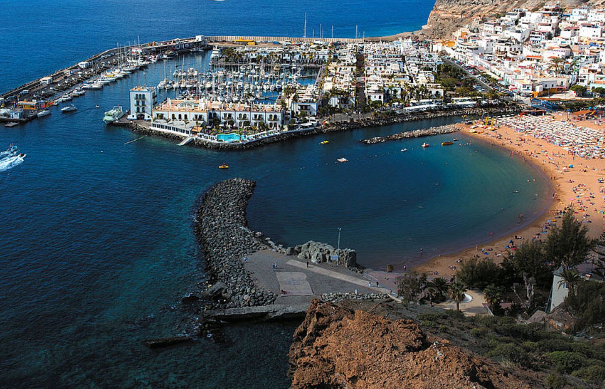 A coastal town with a marina, beach, and rocky coastline.