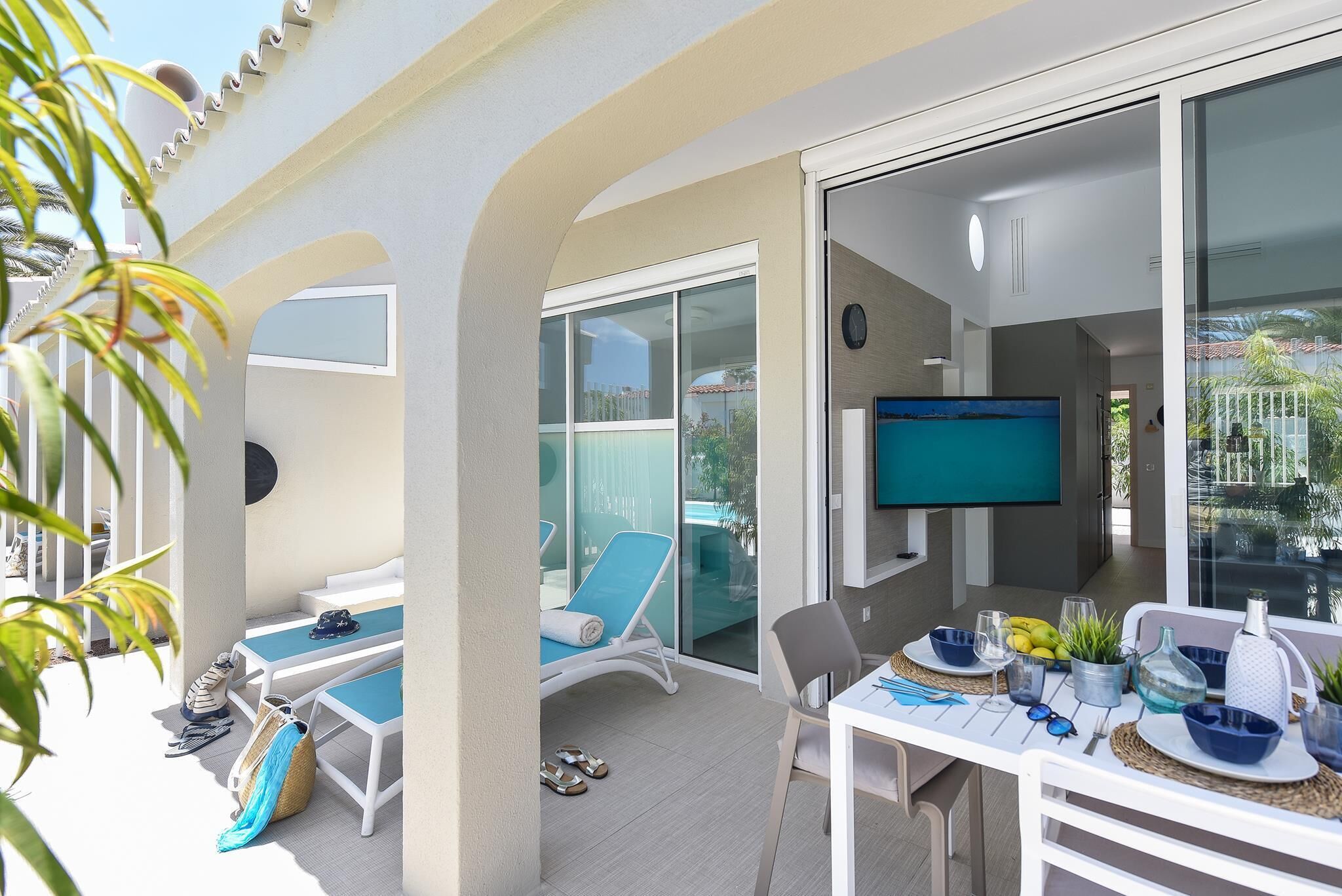 A sunlit patio with a table set for dining, a TV, and lounge chairs.
